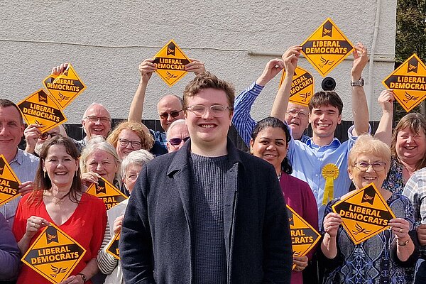 Kieron Franks stood in front of a group of people holding signs that say Liberal Democrats